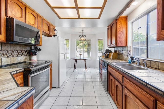 3576 San Jose Ave, Merced, CA 95348 - kitchen with appliances with stainless steel finishes, a sink, tile countertops, decorative backsplash, and decorative light fixtures