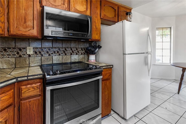 3576 San Jose Ave, Merced, CA 95348 - kitchen with stainless steel appliances, tasteful backsplash, light tile patterned flooring, brown cabinetry, and baseboards