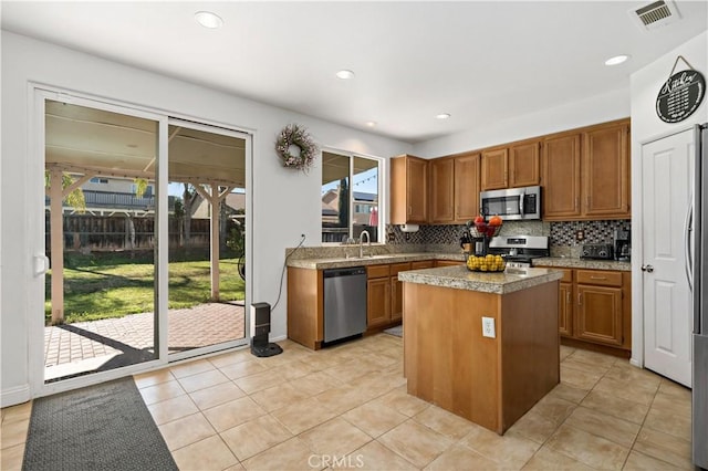 28867 Glencoe Ln, Menifee, CA 92584 - kitchen with appliances with stainless steel finishes, decorative backsplash, brown cabinetry, a kitchen island, and light tile patterned floors