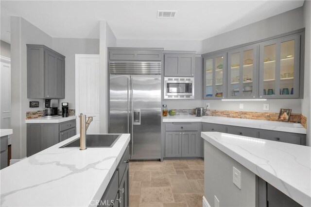 7 Olympic Way, Coto De Caza, CA 92679 - kitchen with built in appliances, gray cabinetry, glass insert cabinets, light stone counters, and light stone finish floors