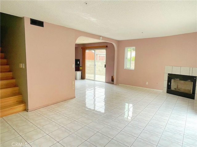3855 Gilman Rd, El Monte, CA 91732 - unfurnished living room with arched walkways, a tiled fireplace, stairway, light tile patterned floors, and a textured ceiling
