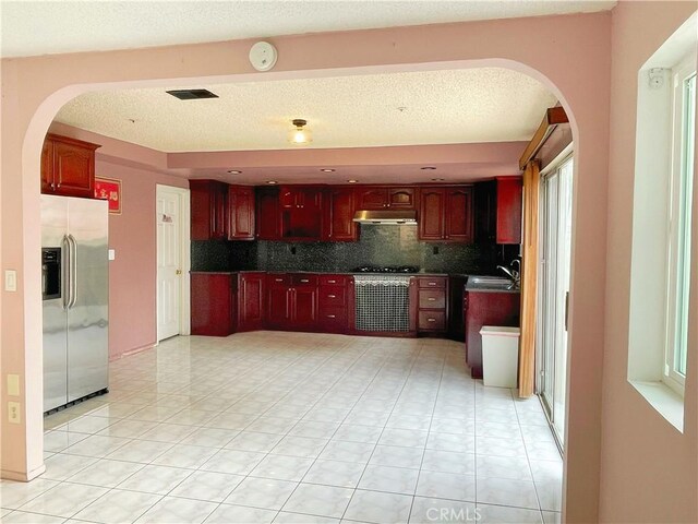 3855 Gilman Rd, El Monte, CA 91732 - kitchen with stainless steel fridge, arched walkways, backsplash, reddish brown cabinets, and a textured ceiling