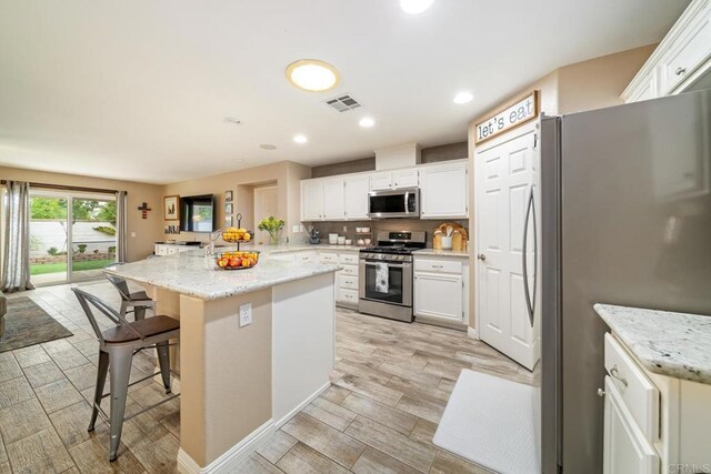 1064 Eliot St, Oceanside, CA 92057 - kitchen with stainless steel appliances, a breakfast bar, wood finish floors, white cabinets, and recessed lighting