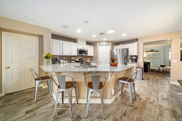 1064 Eliot St, Oceanside, CA 92057 - kitchen featuring appliances with stainless steel finishes, a peninsula, light wood finished floors, white cabinetry, and a breakfast bar