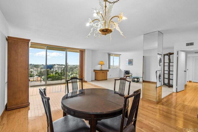 3635 7th Ave Unit 13E, San Diego, CA 92103 - dining room featuring stacked washer and clothes dryer, light wood-type flooring, a wall of windows, and a chandelier