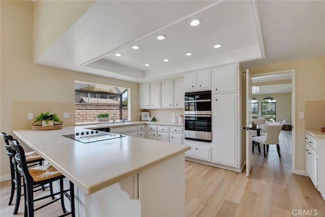 5697 Los Robles, La Verne, CA 91750 - kitchen featuring a tray ceiling, black electric cooktop, a peninsula, light wood finished floors, and a breakfast bar