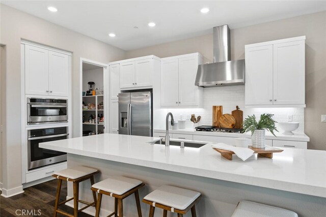 27227 Coyote Bush Ct, Valencia, CA 91381 - kitchen with wall chimney range hood, stainless steel appliances, a sink, a breakfast bar, and dark wood finished floors