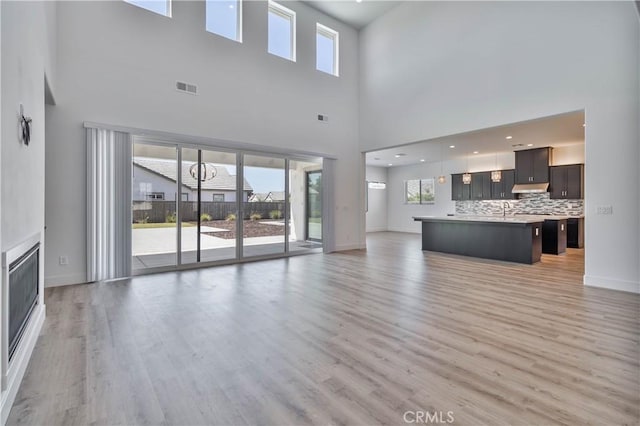 1734 Lester Ave, Clovis, CA 93619 - unfurnished living room featuring light wood-type flooring, a high ceiling, baseboards, and a glass covered fireplace