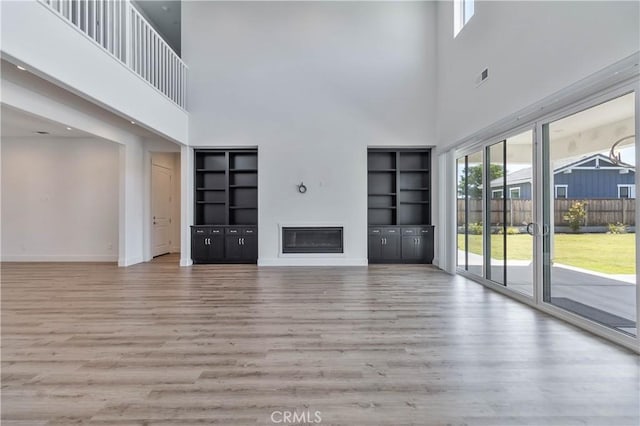 1734 Lester Ave, Clovis, CA 93619 - unfurnished living room featuring a towering ceiling, wood finished floors, baseboards, a glass covered fireplace, and built in shelves
