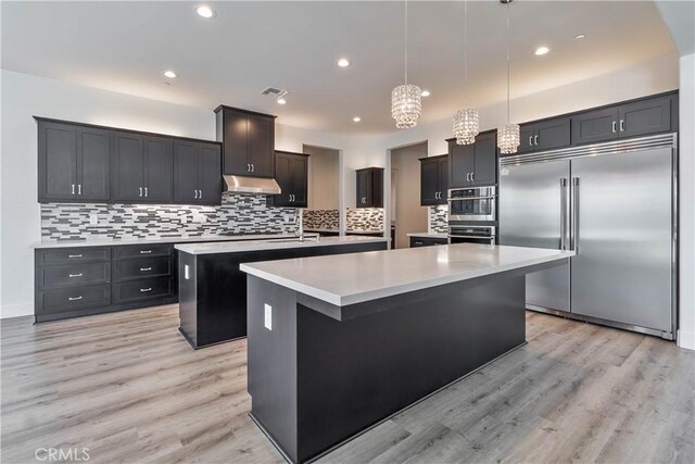 1734 Lester Ave, Clovis, CA 93619 - kitchen with stainless steel appliances, a kitchen island with sink, light wood-style floors, light countertops, and decorative backsplash