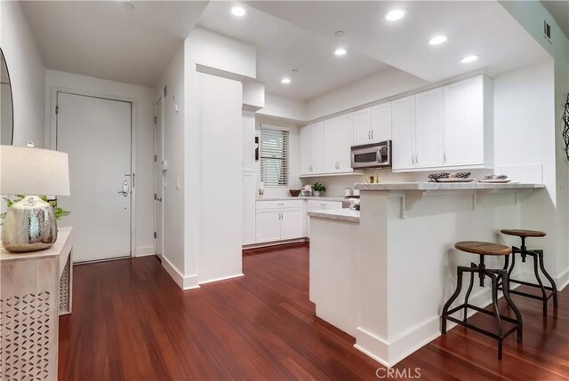 395 E 4th St Unit 13, Long Beach, CA 90802 - kitchen with stainless steel microwave, a breakfast bar, white cabinetry, dark wood finished floors, and recessed lighting