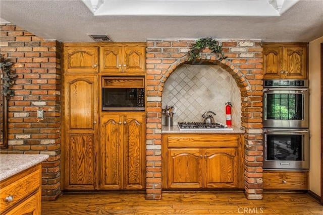 639 Valley View Dr, Redlands, CA 92373 - kitchen with appliances with stainless steel finishes, a textured ceiling, light countertops, brown cabinets, and dark wood-type flooring