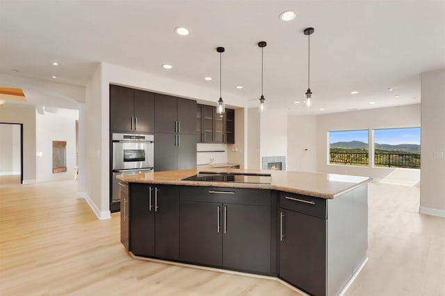 1320 Sleeping Indian Rd, Oceanside, CA 92057 - kitchen featuring black electric cooktop, stainless steel double oven, a center island with sink, light wood finished floors, and decorative light fixtures