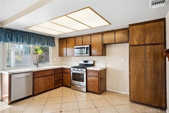 663 Redwood Ave, Upland, CA 91786 - kitchen featuring appliances with stainless steel finishes, brown cabinets, tile counters, a sink, and light tile patterned flooring