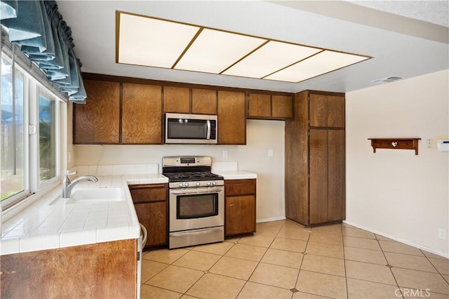 663 Redwood Ave, Upland, CA 91786 - kitchen featuring stainless steel appliances, tile counters, a sink, brown cabinetry, and light tile patterned flooring