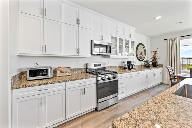18106 Meridian Ln, Saugus, CA 91350 - kitchen featuring appliances with stainless steel finishes, light wood-type flooring, white cabinets, light stone countertops, and glass insert cabinets
