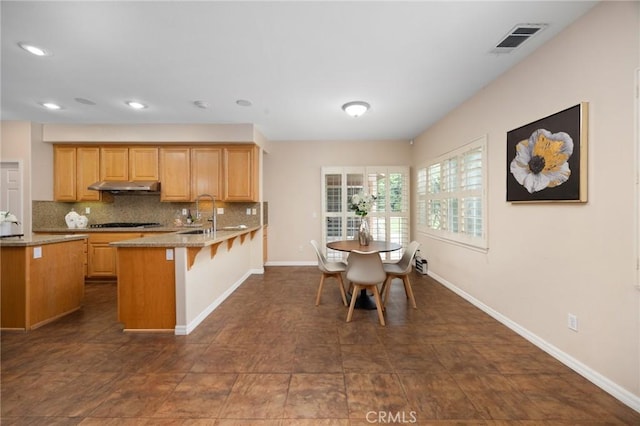 5675 W Overlook Dr, Rancho Cucamonga, CA 91739 - kitchen featuring under cabinet range hood, a peninsula, decorative backsplash, a breakfast bar, and gas cooktop