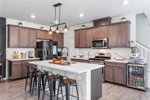 7469 Brahman Ln, Chino, CA 91708 - kitchen featuring appliances with stainless steel finishes, beverage cooler, a sink, light wood-style flooring, and an island with sink
