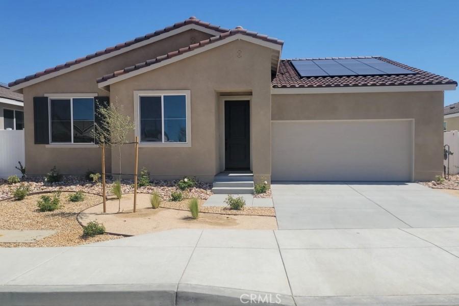 1600 E E Ave H7, Lancaster, CA 93535 - view of front of home featuring stucco siding, an attached garage, roof mounted solar panels, a tiled roof, and driveway