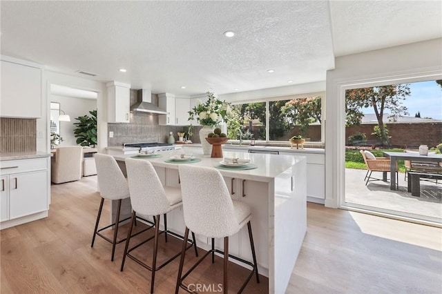 13621 Fairmont Way, Tustin, CA 92780 - kitchen with wall chimney range hood, backsplash, light wood-style floors, white cabinets, and a kitchen breakfast bar