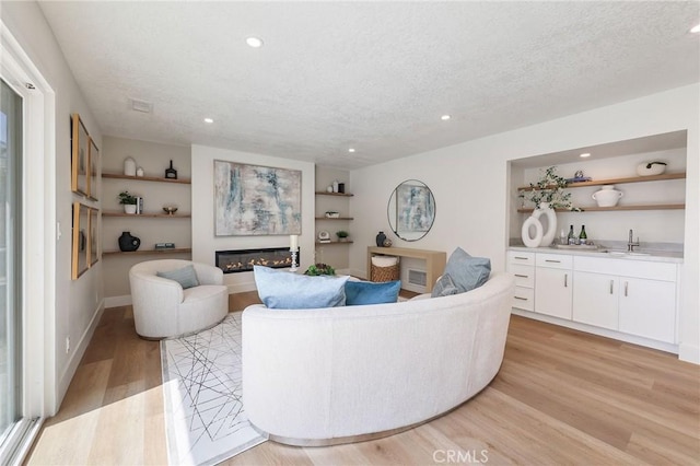 13621 Fairmont Way, Tustin, CA 92780 - living area featuring a textured ceiling, light wood finished floors, a glass covered fireplace, recessed lighting, and built in shelves