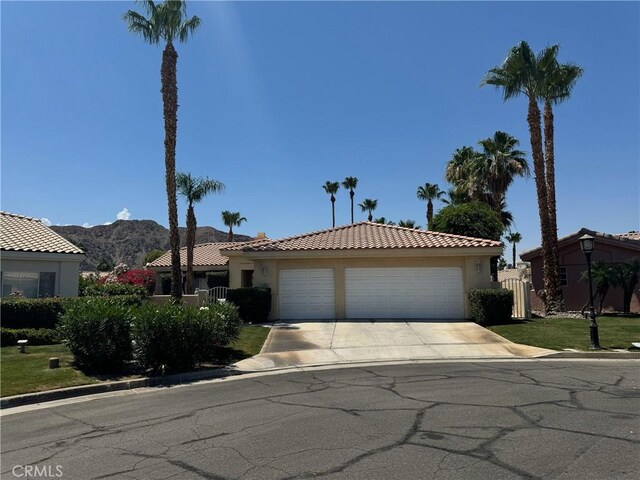 47845 Via Opera Ln, Quinta, CA 92253 - view of front facade with concrete driveway, stucco siding, a tiled roof, a garage, and a mountain view