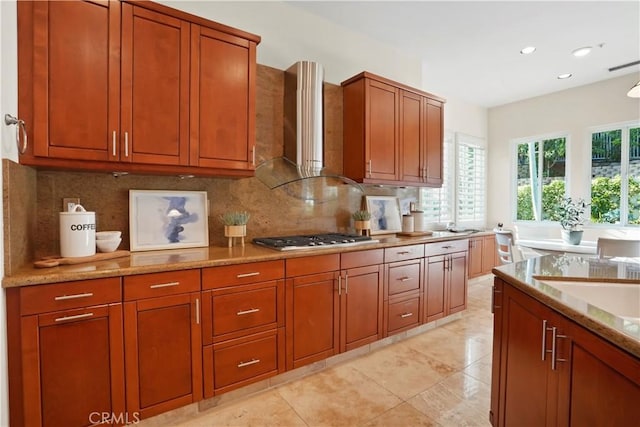 12165 Ojeda Ct, Tustin, CA 92782 - kitchen with stainless steel gas cooktop, wall chimney range hood, tasteful backsplash, brown cabinetry, and light stone countertops