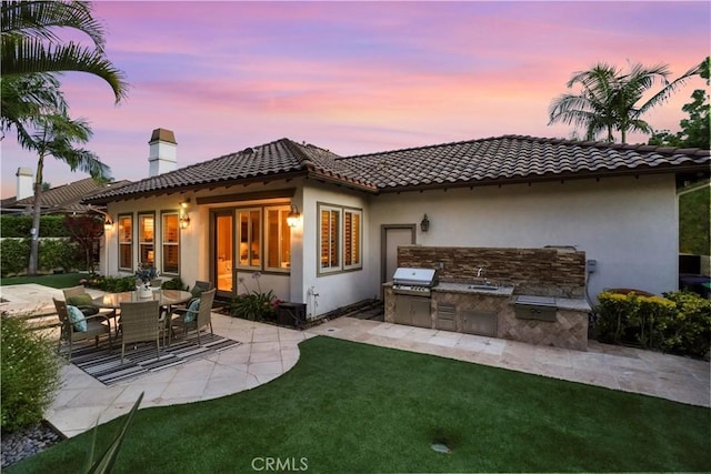 12165 Ojeda Ct, Tustin, CA 92782 - rear view of house featuring exterior kitchen, a chimney, stucco siding, a patio area, and a lawn