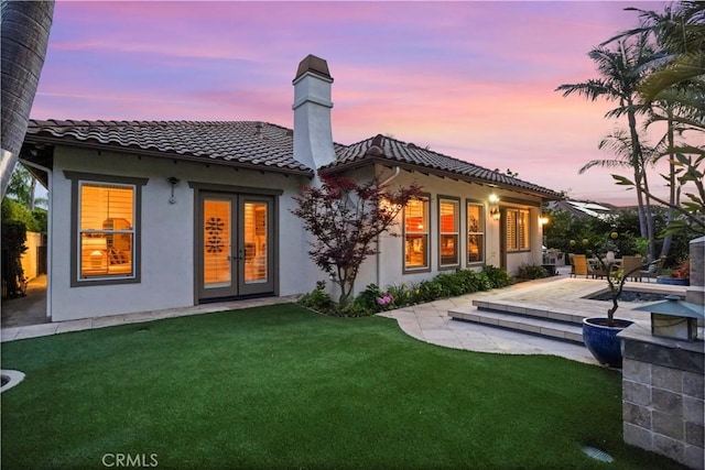 12165 Ojeda Ct, Tustin, CA 92782 - back of property at dusk with a tiled roof, french doors, stucco siding, a chimney, and a yard