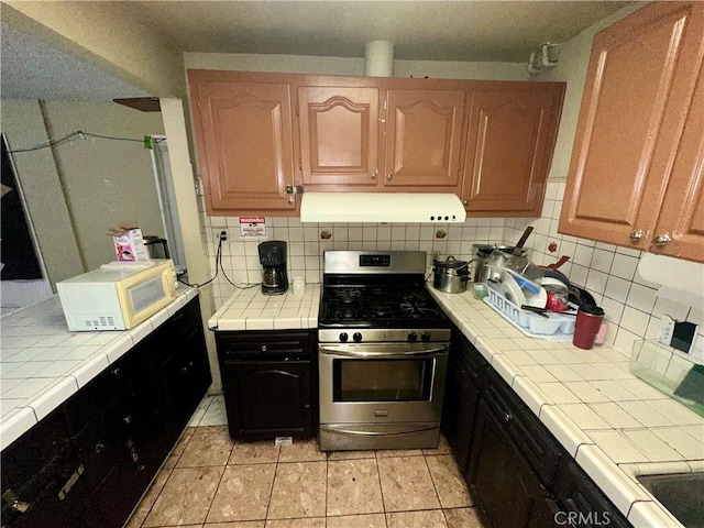 17406 Renault St, La Puente, CA 91744 - kitchen with ventilation hood, gas range, white microwave, tile counters, and decorative backsplash
