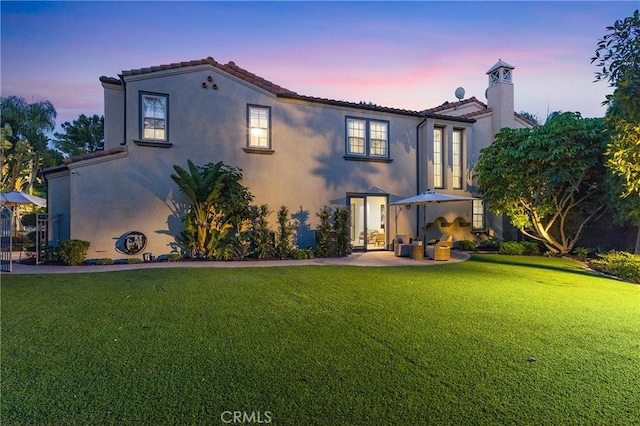 1 Lennox Ct, Ladera Ranch, CA 92694 - back of house at dusk featuring a lawn, stucco siding, a tiled roof, and a chimney