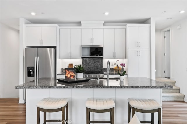 1914 W Bushell St, Anaheim, CA 92805 - kitchen featuring stainless steel microwave, a center island with sink, light wood-style floors, decorative backsplash, and a kitchen bar