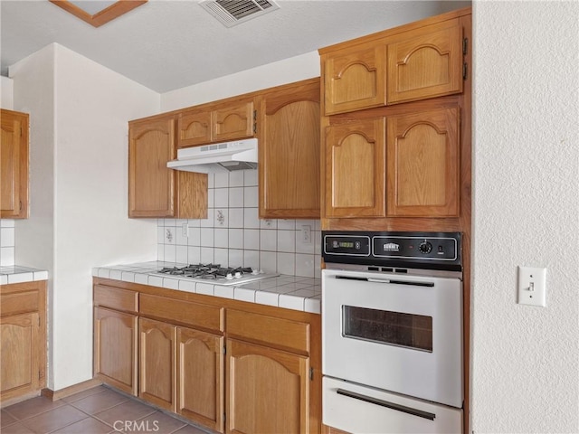 13951 Falling Leaf Rd, Apple Valley, CA 92307 - kitchen with white appliances, a warming drawer, under cabinet range hood, tasteful backsplash, and light tile patterned floors