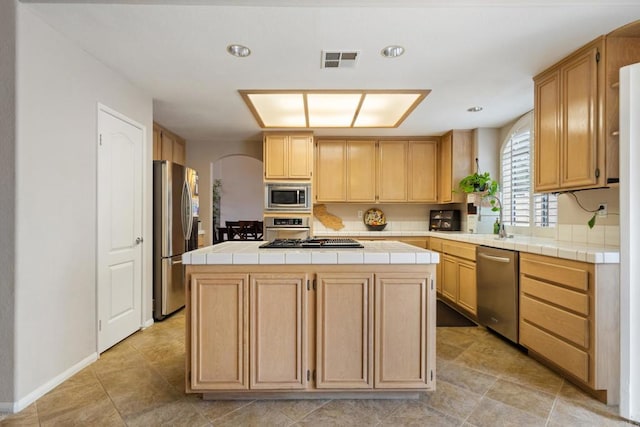 1394 Corte Magna, Oceanside, CA 92057 - kitchen featuring stainless steel appliances, tile counters, a kitchen island, arched walkways, and light brown cabinetry