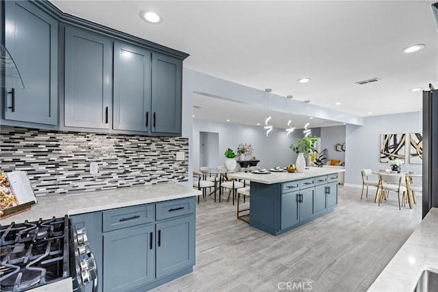 7321 Eglise Ave, Pico Rivera, CA 90660 - kitchen with stainless steel range with gas cooktop, tasteful backsplash, light wood-style floors, a kitchen bar, and decorative light fixtures