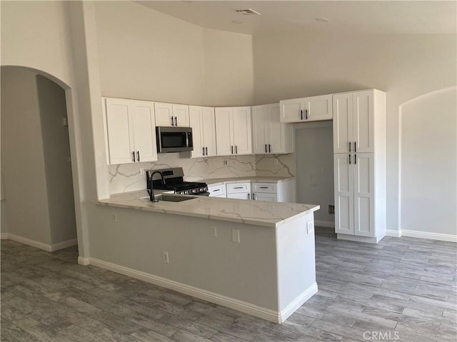 28227 Cobbler Ct, Menifee, CA 92585 - kitchen featuring appliances with stainless steel finishes, high vaulted ceiling, light stone countertops, tasteful backsplash, and white cabinets