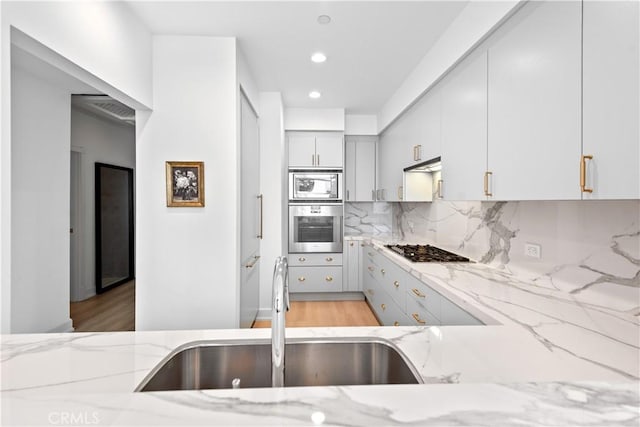 900 W Olympic Blvd Unit 34F, Los Angeles, CA 90015 - kitchen featuring appliances with stainless steel finishes, a sink, light stone counters, backsplash, and light wood-style flooring