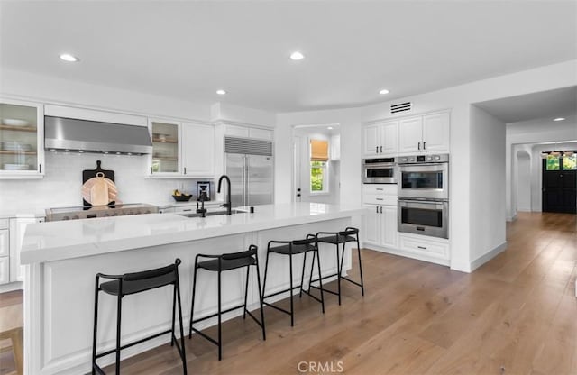 31 Harcourt, Newport Coast, CA 92657 - kitchen featuring wall chimney exhaust hood, appliances with stainless steel finishes, a sink, white cabinetry, and a kitchen island with sink