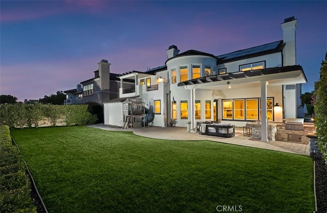 31 Harcourt, Newport Coast, CA 92657 - back of property at dusk featuring area for grilling, a patio area, a lawn, stucco siding, and a chimney
