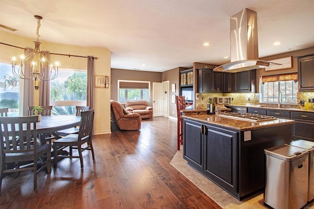 11606 Mesa Verde Dr, Valley Center, CA 92082 - kitchen featuring island exhaust hood, a chandelier, stainless steel gas stovetop, hardwood / wood-style flooring, and backsplash