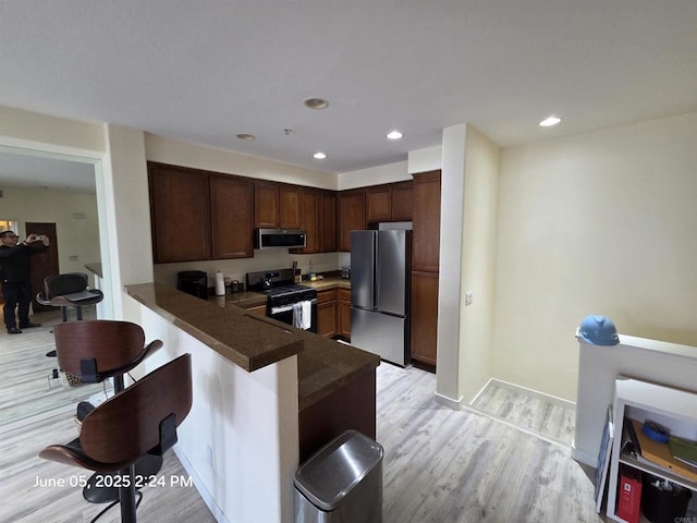 1760 E Palomar St Unit 111, Chula Vista, CA 91913 - kitchen featuring appliances with stainless steel finishes, dark countertops, a peninsula, light wood finished floors, and a breakfast bar