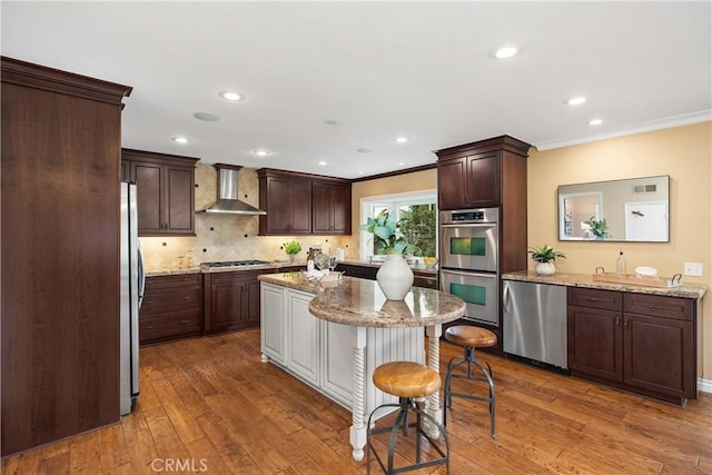 29162 Bobolink Dr, Laguna Niguel, CA 92677 - kitchen with wall chimney exhaust hood, appliances with stainless steel finishes, dark brown cabinetry, hardwood / wood-style floors, and a center island