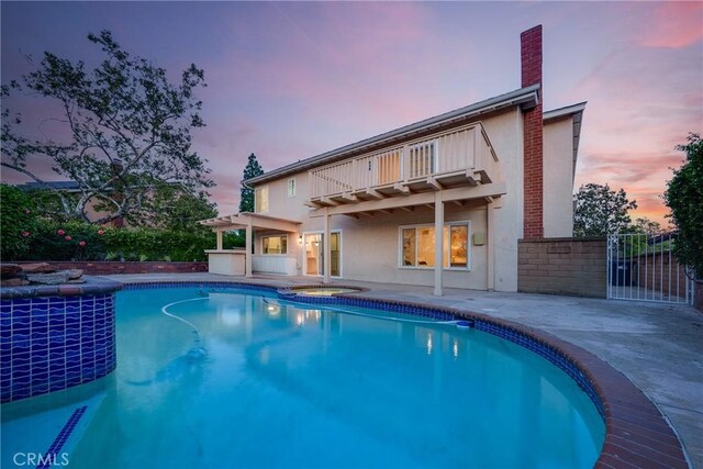 27591 Cenajo, Mission Viejo, CA 92691 - back of property at dusk featuring a balcony, stucco siding, a patio area, a chimney, and a pool with connected hot tub