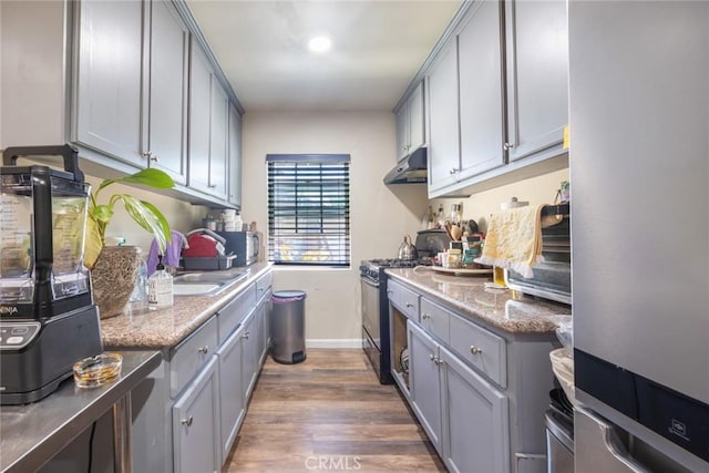 11100 S Normandie Ave, Los Angeles, CA 90044 - kitchen with stainless steel appliances, under cabinet range hood, gray cabinets, baseboards, and dark wood finished floors
