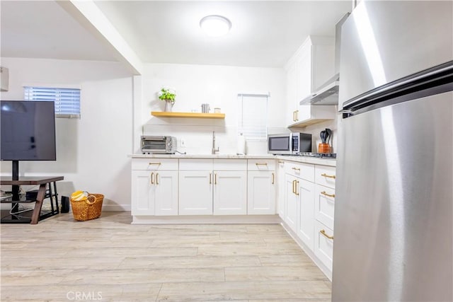 3720 S St Andrews Pl, Los Angeles, CA 90018 - kitchen with appliances with stainless steel finishes, under cabinet range hood, white cabinets, light wood-style floors, and light countertops