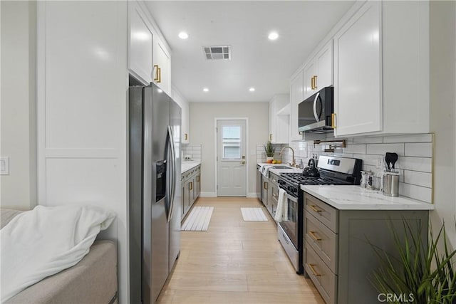 1217 W 77th St, Los Angeles, CA 90044 - kitchen featuring appliances with stainless steel finishes, light wood-style floors, tasteful backsplash, white cabinetry, and recessed lighting
