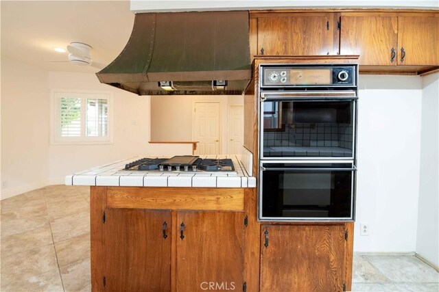 10425 Hillview Ave, Chatsworth, CA 91311 - kitchen featuring double wall oven, stainless steel gas stovetop, wall chimney exhaust hood, tile counters, and baseboards