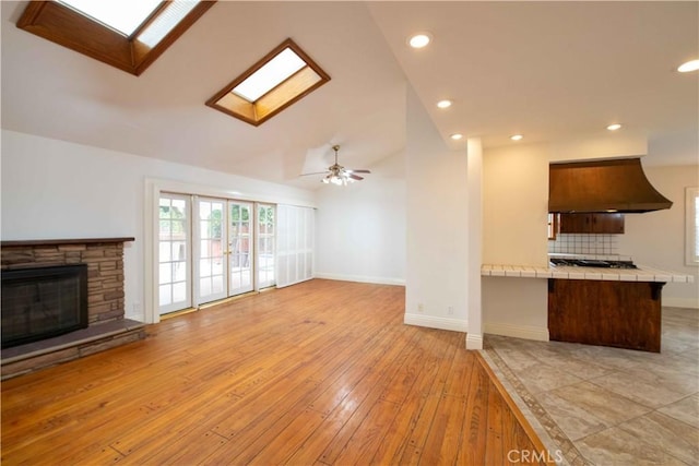 10425 Hillview Ave, Chatsworth, CA 91311 - unfurnished living room featuring a skylight, healthy amount of natural light, lofted ceiling, light wood-style flooring, and a stone fireplace