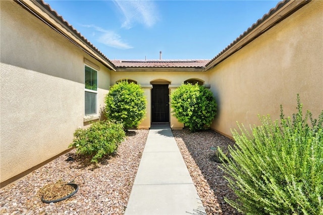 6875 Adainville Dr, Palmdale, CA 93552 - view of exterior entry featuring stucco siding, roof mounted solar panels, and a tiled roof