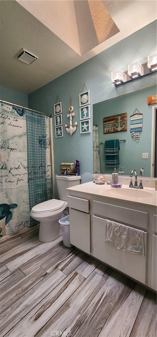 15009 Hopland St, Victorville, CA 92394 - bathroom with toilet, vanity, wood finished floors, a textured ceiling, and a shower with curtain